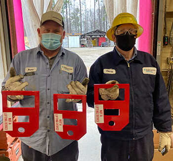 Two SIC team members holding up custom-made load securement devices